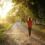 Mujer de espaldas con sudadera roja caminando sola por un camino de tierra al atardecer