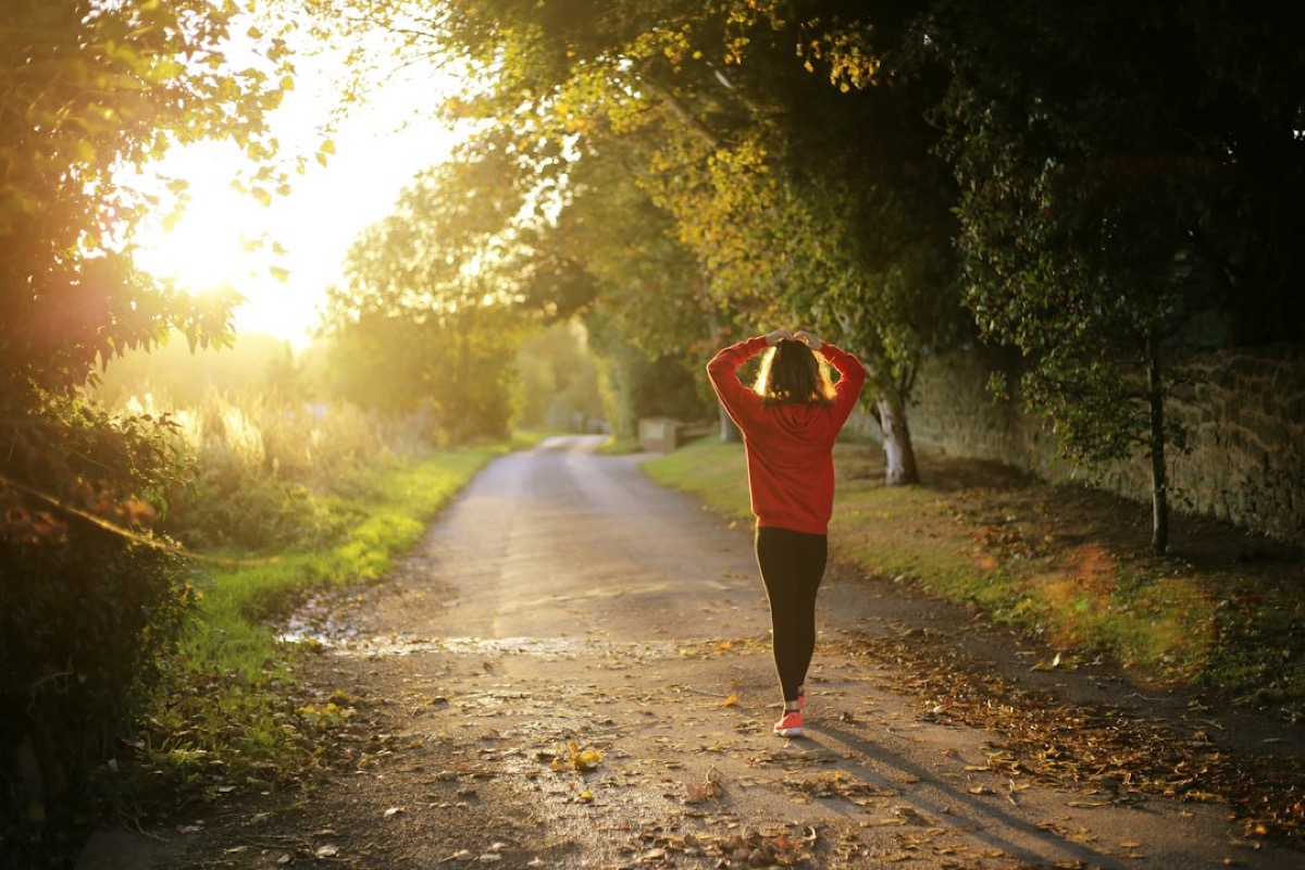 Mujer de espaldas con sudadera roja caminando sola por un camino de tierra al atardecer